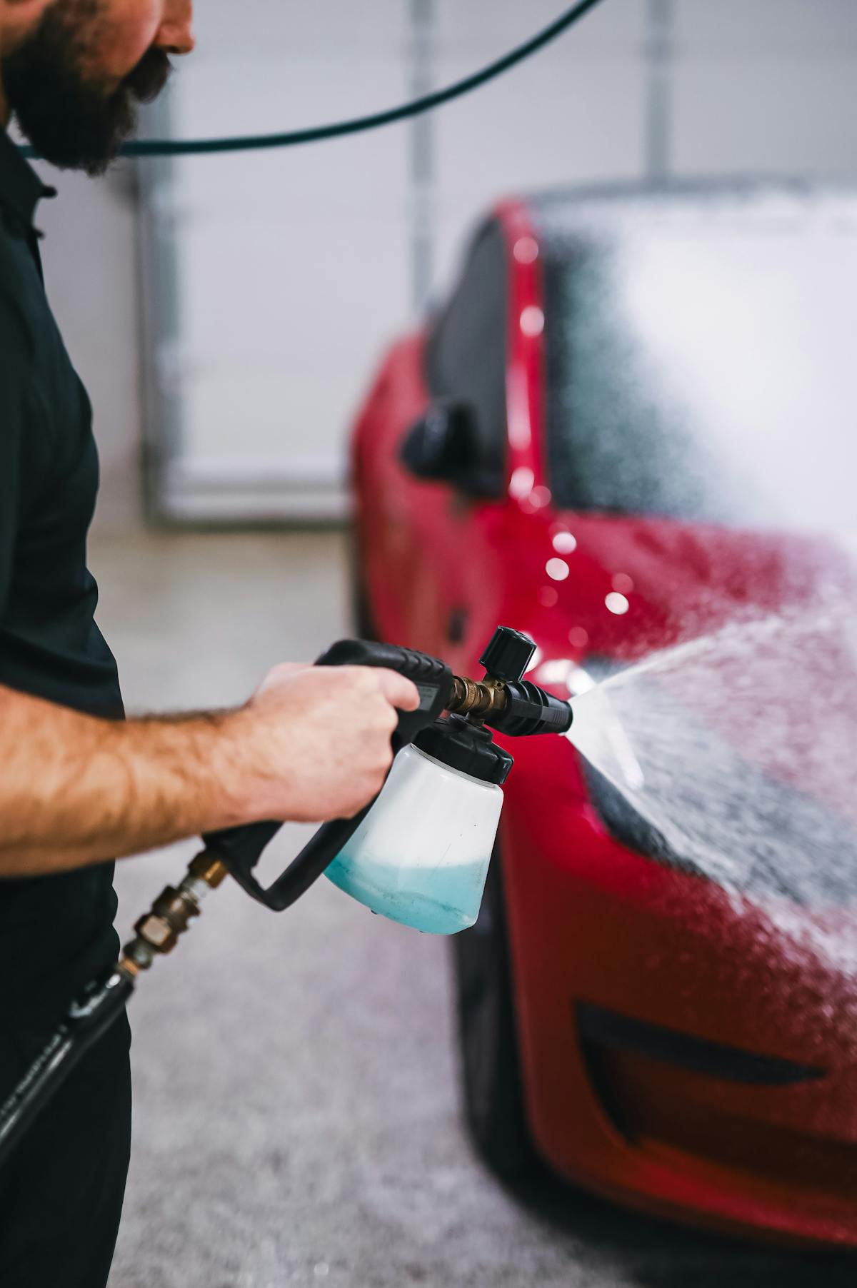 Mano guantata che applica spray nanotecnologico sulla carrozzeria lucida con panno in microfibra